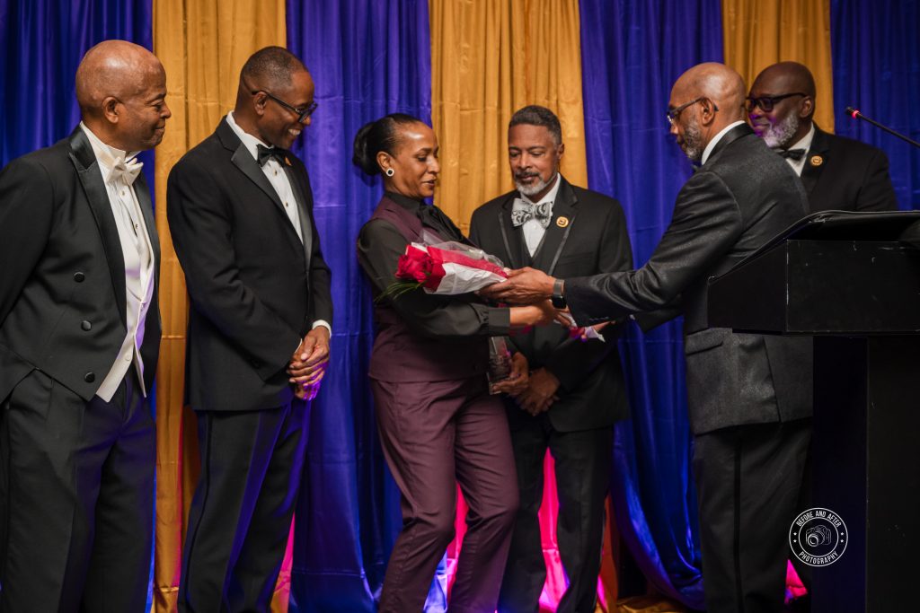Lana Reid accepts a bouquet of red roses from a member of the Eta Nu Nu Chapter of Omega Psi Phi Fraternity, Inc. as fellow fraternity brothers look on during the 2025 Achievement Week Humanitarian Award ceremony.