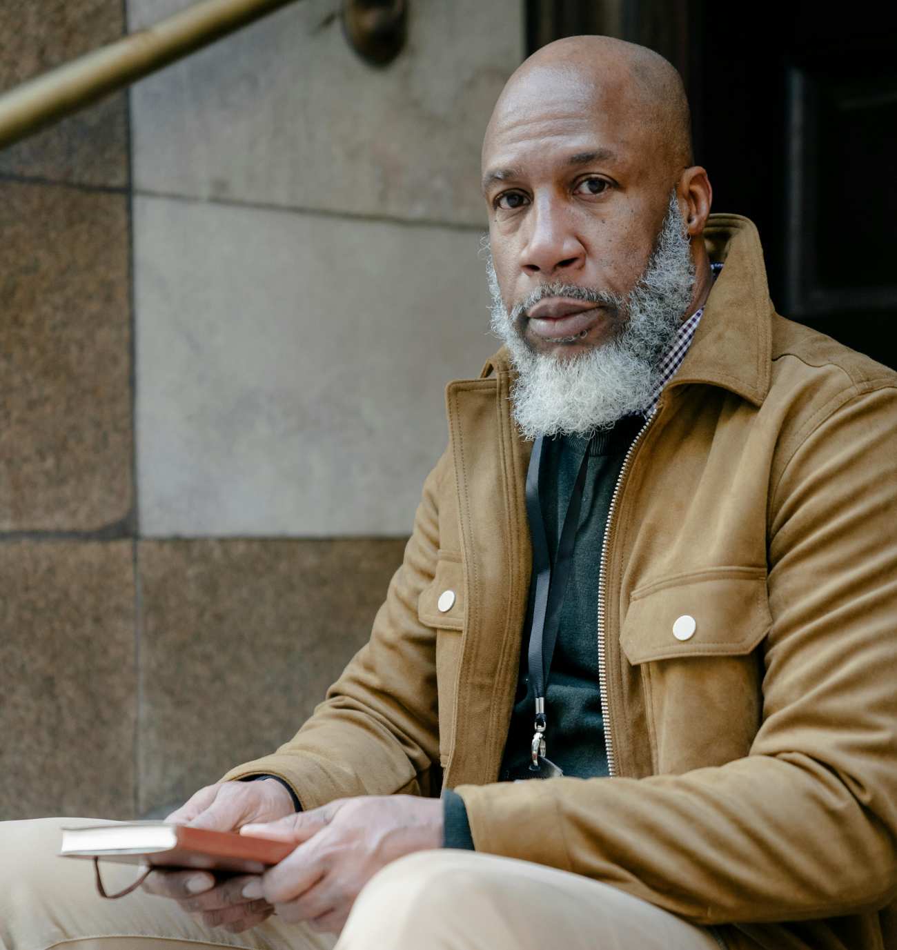 Black man seated outdoors holding a notebook, appearing thoughtful