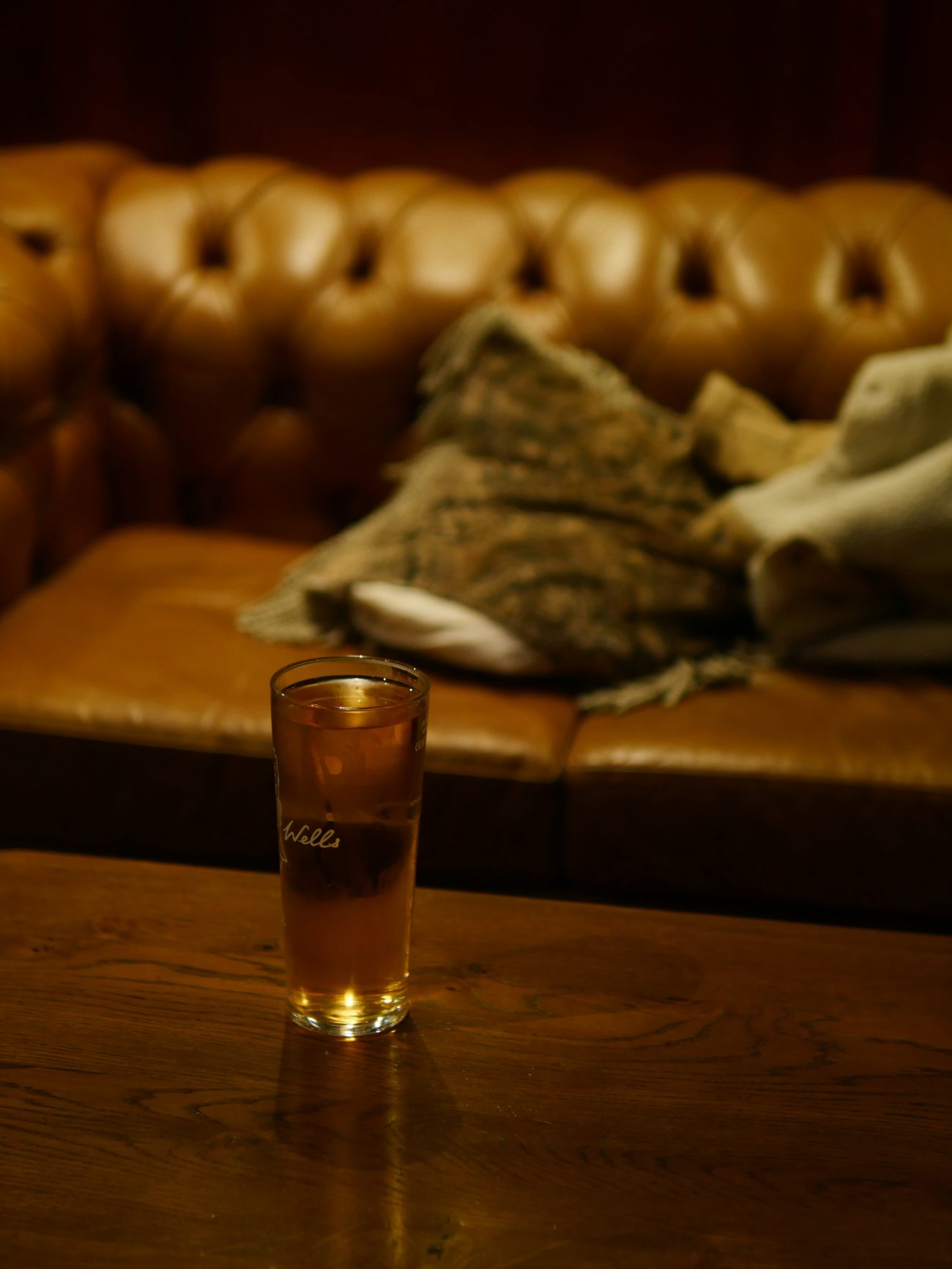 A glass of ginger ale on a wooden table in front of a couch and blanket, reflecting themes of comfort, memory, and healing in Black households.